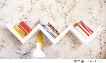 Zigzag bookshelf with books on a light wall Zigzag bookshelf with books on a light wall 137211198