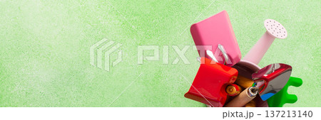 Colorful gardening tools arranged in a small bucket on a green surface ready for spring planting, banner Colorful gardening tools arranged in a small bucket on a green surface ready for spring planting, banner 137213140
