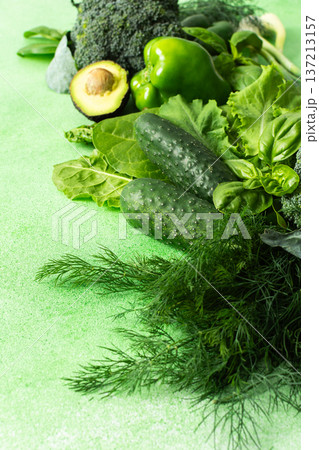A variety of fresh green vegetables and herbs are arranged neatly on a bright green surface. Among them are cucumbers, broccoli, leafy greens, avocado, and basil, perfect for healthy cooking or salads A variety of fresh green vegetables and herbs are arranged neatly on a bright green surface. Among them are cucumbers, broccoli, leafy greens, avocado, and basil, perfect for healthy cooking or salads 137213157