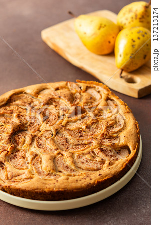 A fresh pear pie is placed on a cloth on a table. Nearby, a bowl holds ripe pears and a small vase has flowers. The setting looks warm and inviting for sharing a treat A fresh pear pie is placed on a cloth on a table. Nearby, a bowl holds ripe pears and a small vase has flowers. The setting looks warm and inviting for sharing a treat 137213174