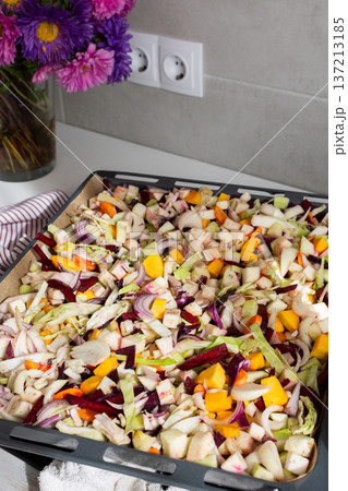 Fresh vegetables are chopped and placed on a baking tray ready for cooking in the oven. Colorful ingredients are showcased, and the setting is a welcoming kitchen Fresh vegetables are chopped and placed on a baking tray ready for cooking in the oven. Colorful ingredients are showcased, and the setting is a welcoming kitchen 137213185