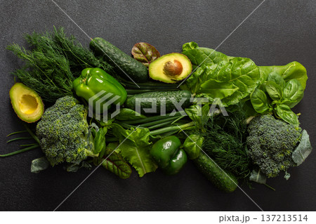 Various green vegetables such as broccoli, cucumbers, green peppers, and lettuce, fresh herbs like basil and dill, along with ripe avocado are artfully arranged on a dark background, healthy meal Various green vegetables such as broccoli, cucumbers, green peppers, and lettuce, fresh herbs like basil and dill, along with ripe avocado are artfully arranged on a dark background, healthy meal 137213514