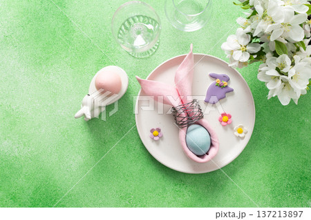 A beautifully arranged table setting for Easter features a pink napkin wrapped around an egg, surrounded by floral decorations and colorful candies A beautifully arranged table setting for Easter features a pink napkin wrapped around an egg, surrounded by floral decorations and colorful candies 137213897