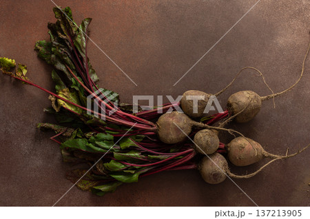 Beets with green leaves rest on a brown surface in a kitchen. The setting is warm and hints at fresh produce ready for cooking or eating 137213905