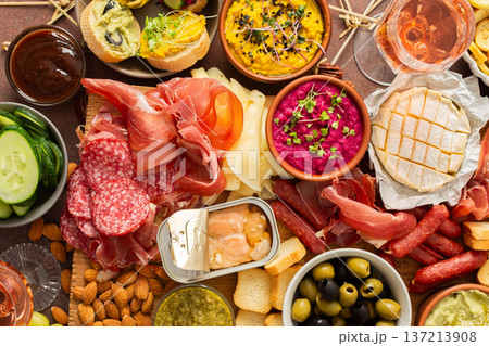 Enjoy a vibrant charcuterie board filled with assorted cheeses, savory sausages, creamy hummus, nuts, and colorful vegetables. Perfect for sharing at a casual gathering 137213908