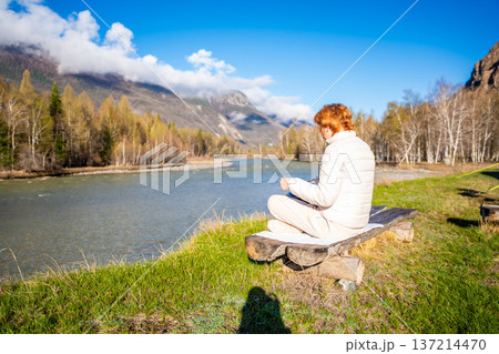 Woman playing a steel tongue drum in nature with a mountain river and Altai landscape in the background. Concept of harmony, mindfulness, and connection with nature Woman playing a steel tongue drum in nature with a mountain river and Altai landscape in the background. Concept of harmony, mindfulness, and connection with nature 137214470