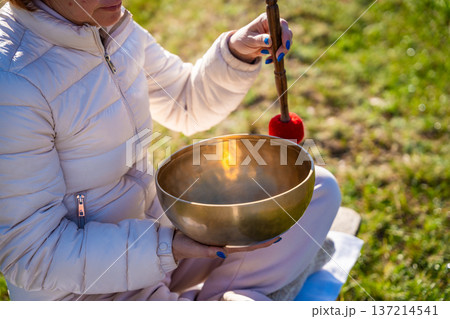 Close-up of hands playing a Tibetan singing bowl by a mountain river. Concept of sacred vibration, healing through touch, and meditative connection to natural energy 137214541