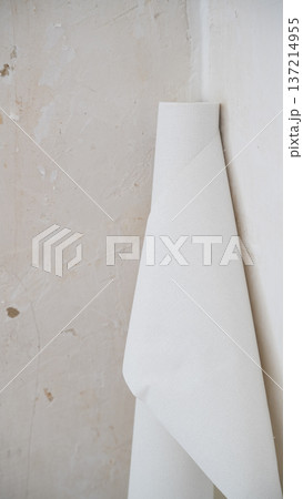Rolled white wallpaper sheet leaning against unfinished plastered wall during interior remodeling project Rolled white wallpaper sheet leaning against unfinished plastered wall during interior remodeling project 137214955