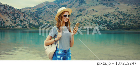 Summer vacation, happy young woman tourist using mobile phone on lake and mountains background Summer vacation, happy young woman tourist using mobile phone on lake and mountains background 137215247