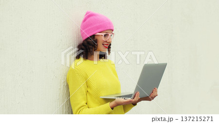 Happy modern young woman working on laptop, freelancer girl looking at computer in colorful clothes 137215271