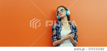 Modern young woman listening to music with smartphone, girl in headphones holding phone 137215282