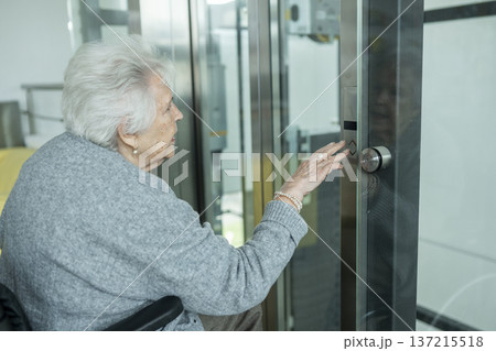 Senior woman in wheelchair entering glass elevator. Senior woman in wheelchair entering glass elevator. 137215518