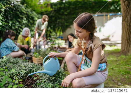 Portrait of cute schoolgirl taking care of plants in school garden during at outdoor sustainable education class. Concept of experiential learning and ecoliteracy. Portrait of cute schoolgirl taking care of plants in school garden during at outdoor sustainable education class. Concept of experiential learning and ecoliteracy. 137215671