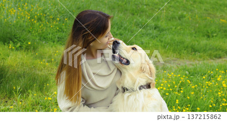 Happy owner young woman with Golden Retriever dog sitting on grass together in summer park 137215862