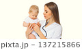 Young woman doctor holding baby and listens to his heart standing on white background 137215866