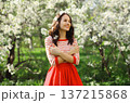 Lovely happy smiling young woman in spring blooming garden with white flowers on the trees in park 137215868