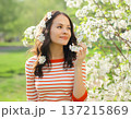 Lovely happy smiling young woman in spring blooming garden with white flowers on the trees in park 137215869