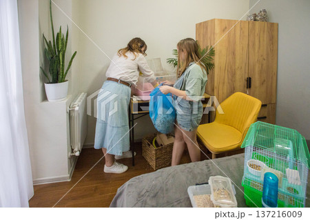 Mom and daughter work together to clean a pet hamster cage in a cozy room. Mom and daughter work together to clean a pet hamster cage in a cozy room. 137216009