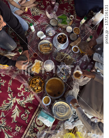 Realistic top view photograph of a traditional Arab family gathering around the table while preparing and sharing iftar during Ramadan. Authentic Ramadan atmosphere, traditional dishes, cultural 137216131