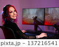 Smiling young woman with vibrant hair streaming gameplay with dual monitors 137216541