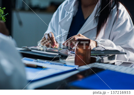 Medical team having a meeting with doctors in white lab coats and surgical scrubs seated at a table discussing a patients working online using computers in the medical industry. Medical team having a meeting with doctors in white lab coats and surgical scrubs seated at a table discussing a patients working online using computers in the medical industry. 137216933