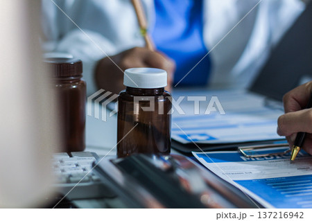 Medical team having a meeting with doctors in white lab coats and surgical scrubs seated at a table discussing a patients working online using computers in the medical industry. Medical team having a meeting with doctors in white lab coats and surgical scrubs seated at a table discussing a patients working online using computers in the medical industry. 137216942