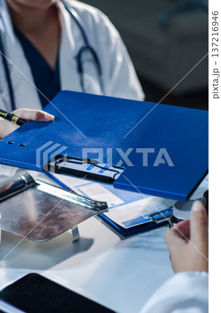 Medical team having a meeting with doctors in white lab coats and surgical scrubs seated at a table discussing a patients working online using computers in the medical industry. Medical team having a meeting with doctors in white lab coats and surgical scrubs seated at a table discussing a patients working online using computers in the medical industry. 137216946
