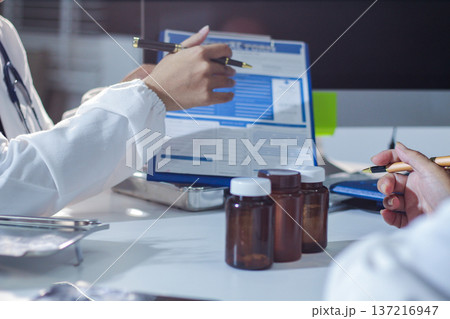 Medical team having a meeting with doctors in white lab coats and surgical scrubs seated at a table discussing a patients working online using computers in the medical industry. 137216947