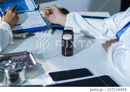 Medical team having a meeting with doctors in white lab coats and surgical scrubs seated at a table discussing a patients working online using computers in the medical industry. Medical team having a meeting with doctors in white lab coats and surgical scrubs seated at a table discussing a patients working online using computers in the medical industry. 137216948