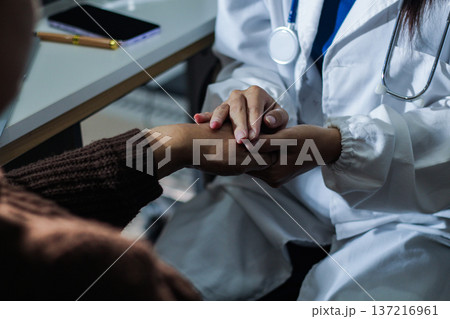 Senior patient lying in hospital bed receiving comforting touch from young female nurse, hands gently clasped together, medical care setting visible Senior patient lying in hospital bed receiving comforting touch from young female nurse, hands gently clasped together, medical care setting visible 137216961