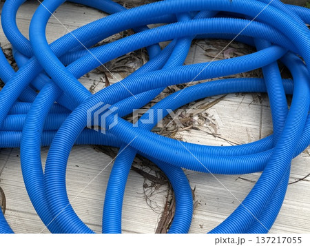 Blue corrugated pipes scattered over leaves and wooden deck creating abstract background 137217055