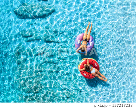 Aerial view of beautiful young women on swim rings in blue sea Aerial view of beautiful young women on swim rings in blue sea 137217238
