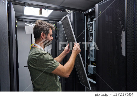 IT technician performing server maintenance in a data center rack replacing air filter panel IT technician performing server maintenance in a data center rack replacing air filter panel 137217504