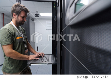IT technician working on server rack with laptop in a modern data center server room 137217512