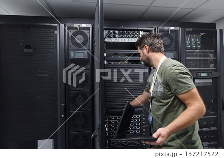 IT technician working on servers in a data center with laptop performing maintenance and monitoring 137217522
