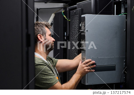 IT technician installing server hardware in a data center rack performing maintenance and network setup IT technician installing server hardware in a data center rack performing maintenance and network setup 137217574