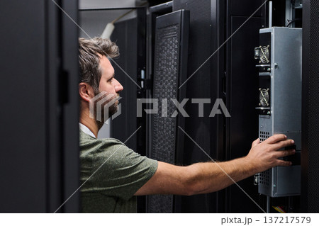 It technician servicing a server rack in a data center performing hardware maintenance and inspection 137217579