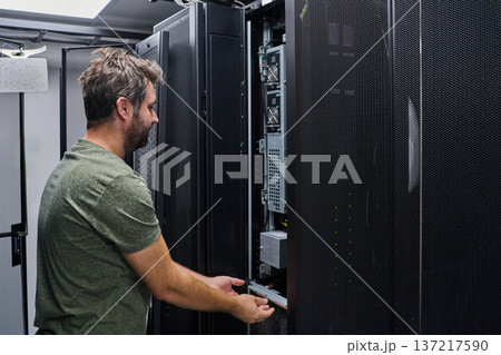 IT technician performing server maintenance in a data center rack during routine equipment inspection IT technician performing server maintenance in a data center rack during routine equipment inspection 137217590