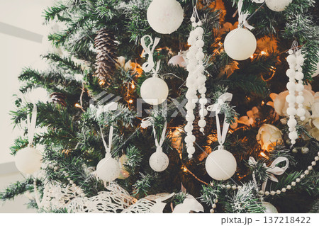 Winter holidays atmosphere background. Closeup of beautifully decorated fir tree with modern white baubles, beards and shiny garland. Christmas and new year magic at home with copy space 137218422