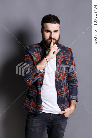 Bearded man shows hush be quiet. Handsome hipster holding finger at his lips, gray studio background, copy space. Secret, privacy concept Bearded man shows hush be quiet. Handsome hipster holding finger at his lips, gray studio background, copy space. Secret, privacy concept 137218434