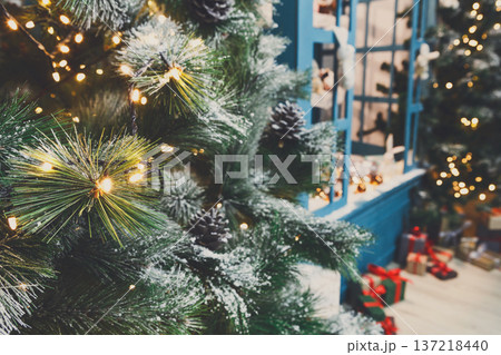 Decorated christmas trees background. Fluffy green pines in shiny garland and beautifully wrapped presents. Xmas and new year eve atmosphere, closeup, copy space 137218440