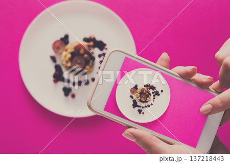 Top view close-up of female hands making flat lay food photo with phone. Oatmeal porridge on pink background, mockup, template, copy space, shallow depth of field Top view close-up of female hands making flat lay food photo with phone. Oatmeal porridge on pink background, mockup, template, copy space, shallow depth of field 137218443