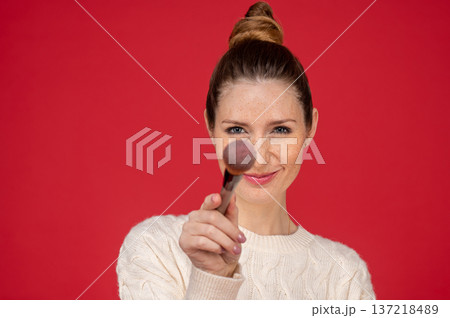 Beautician holding a face brush while standing on red background 137218489