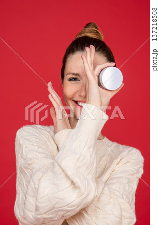 Beautiful young woman on red background with a jar of cream in hand Beautiful young woman on red background with a jar of cream in hand 137218508