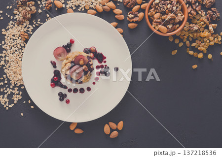 Healthy eating, dieting and detox concept - wholegrain fresh oatmeal porridge on plate with fruits, berries and nuts on dark background. Still life, top view. 137218536
