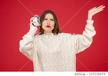Cute young woman on red background with an alarm-clock in hands Cute young woman on red background with an alarm-clock in hands 137218574