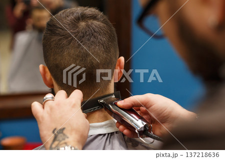 Barber make haircut with trimmer hair clipper in barbershop, closeup of client's head. Hairstyle in male hair salon Barber make haircut with trimmer hair clipper in barbershop, closeup of client's head. Hairstyle in male hair salon 137218636