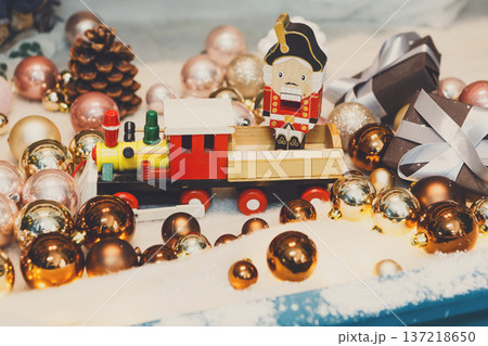 Christmas gifts background. Vintage wooden toy train and nutcracker on snow with golden shiny baubles and small present boxes. Magical atmosphere of new year eve, closeup 137218650