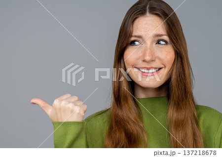 Waist up of a smiling young woman in green clothes pointing to the right with her big finger 137218678