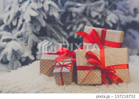 Christmas gifts decorated with red ribbon bows on soft fluffy carpet at blurred snowy fir tree background, closeup, selective focus. Winter holidays concept 137218732